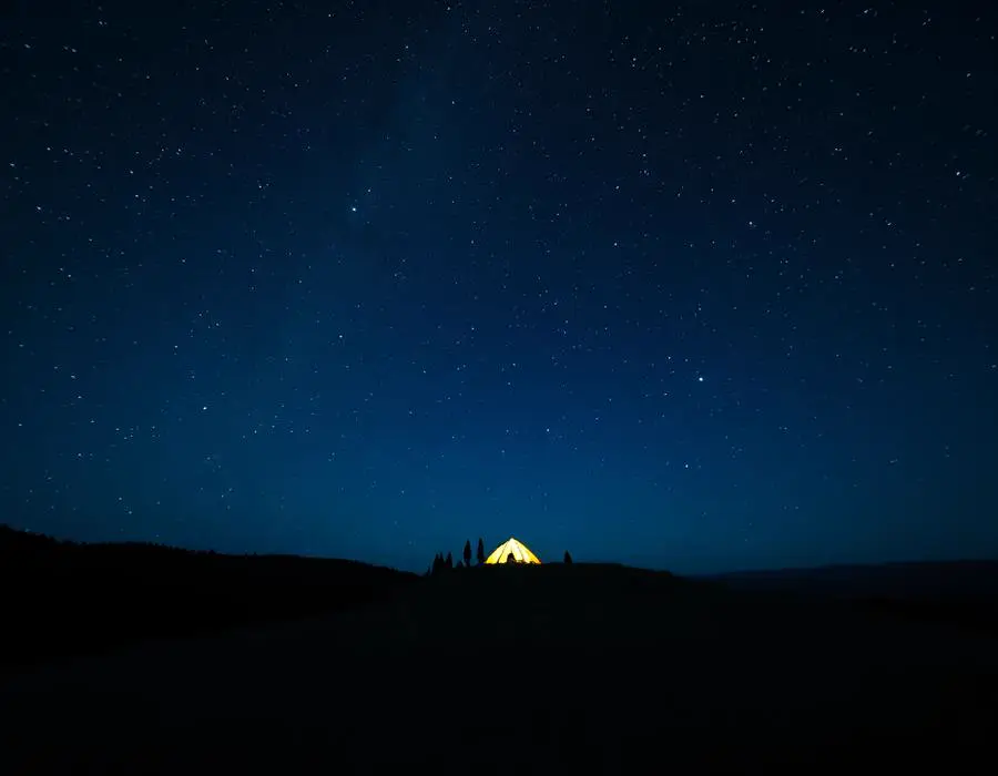 A glowing tent on a hilltop under a sky full of stars