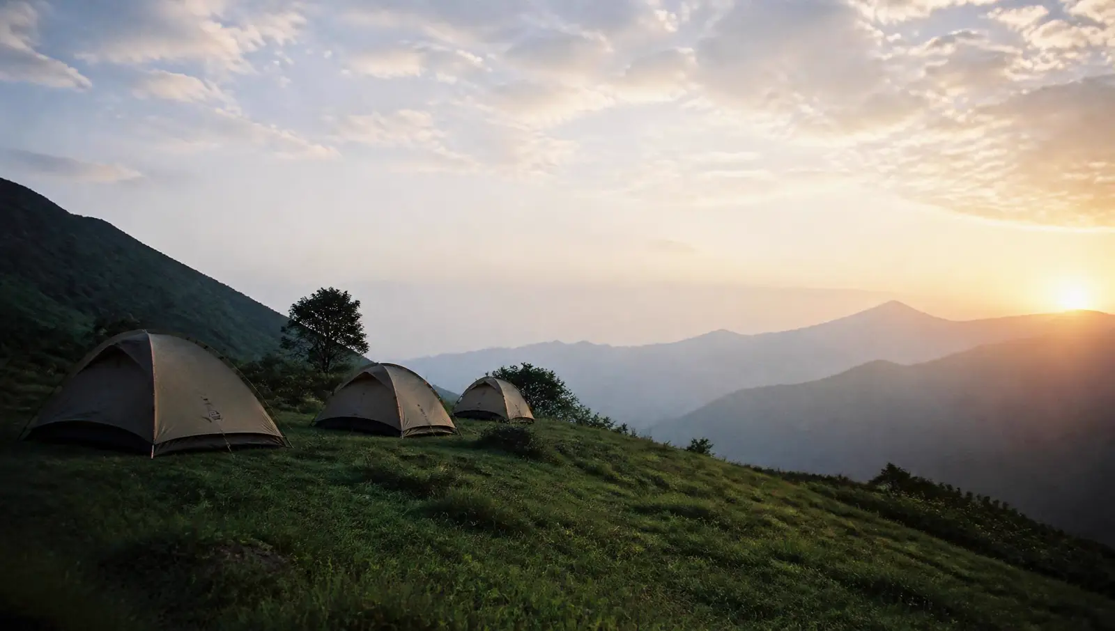 Tents pitched on a grassy ridge overlooking misty mountains at sunrise